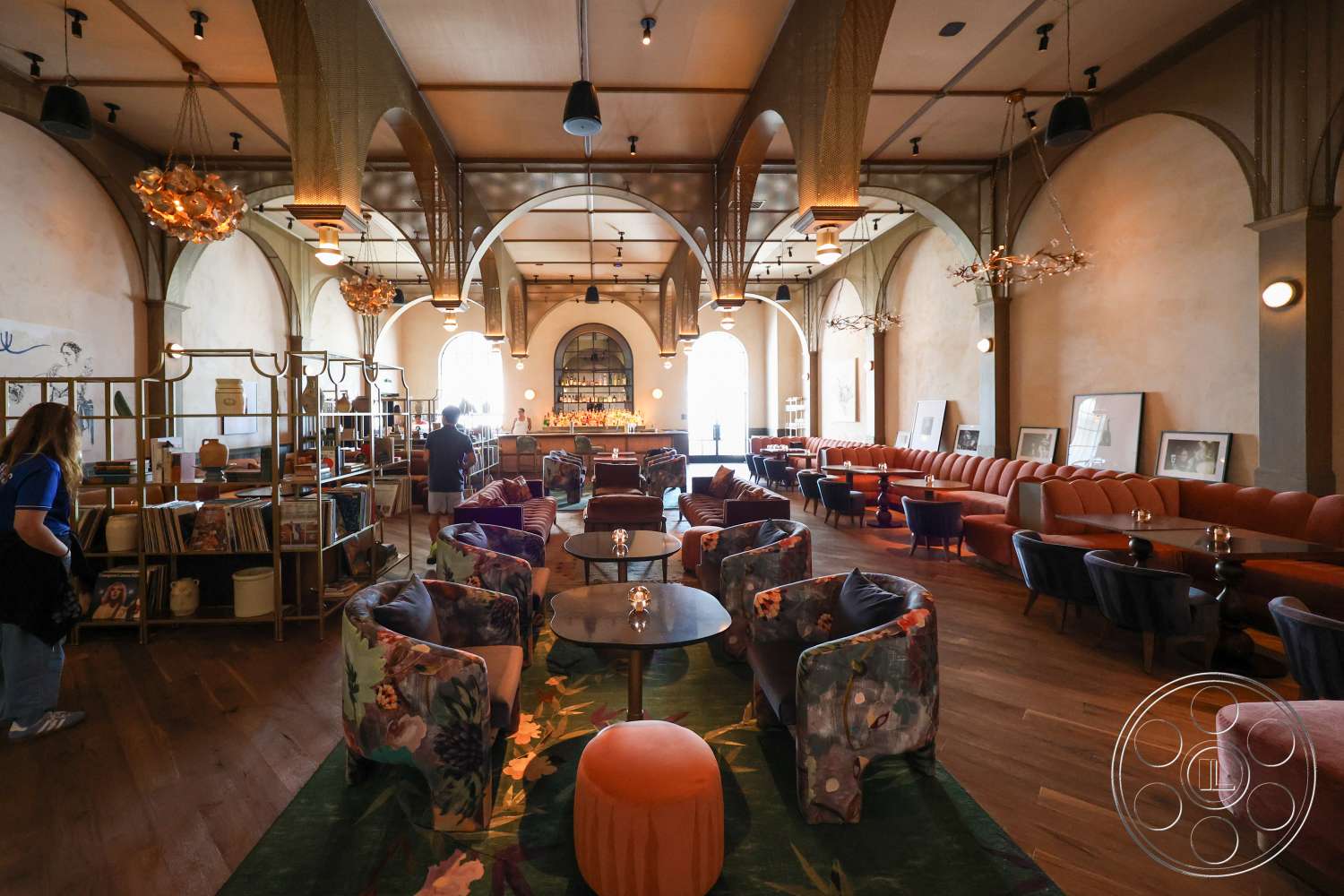 Club 74 - wood flooring, plush seating, decorative wall art, vaulted ceiling, textured plaster walls, soft lighting fixtures, arched windows, upholstered armchairs, exposed wood ceiling beams, interior lounge area, colorful patterned upholstery, rounded coffee tables, bar area with shelving, ambient chandeliers