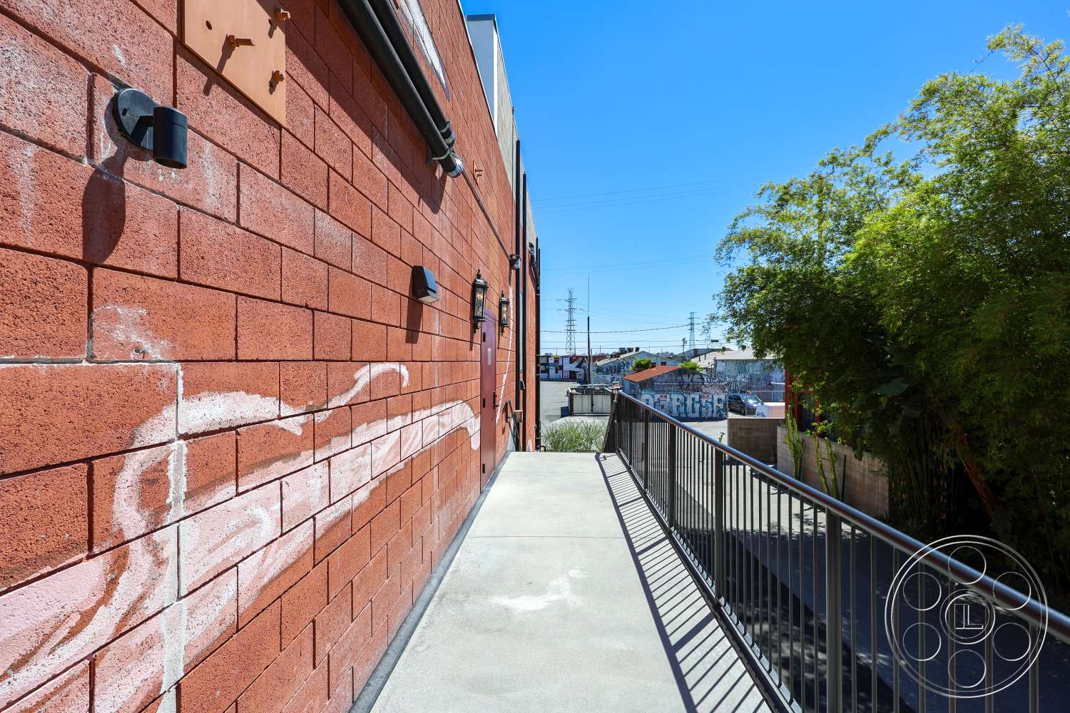 Club 74 - exterior, metal railing, urban setting, concrete walkway, clear blue sky, graffiti wall art, decorative wall lighting, red concrete block walls, landscaped bamboo area