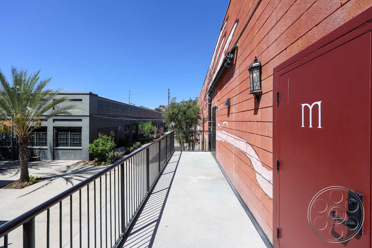 Club 74 - exterior, urban setting, exposed brick wall, commercial building, metal handrail, textured concrete wall, palm tree landscaping, decorative wall mural, red painted door, flat concrete balcony flooring, black wall-mounted light fixtures