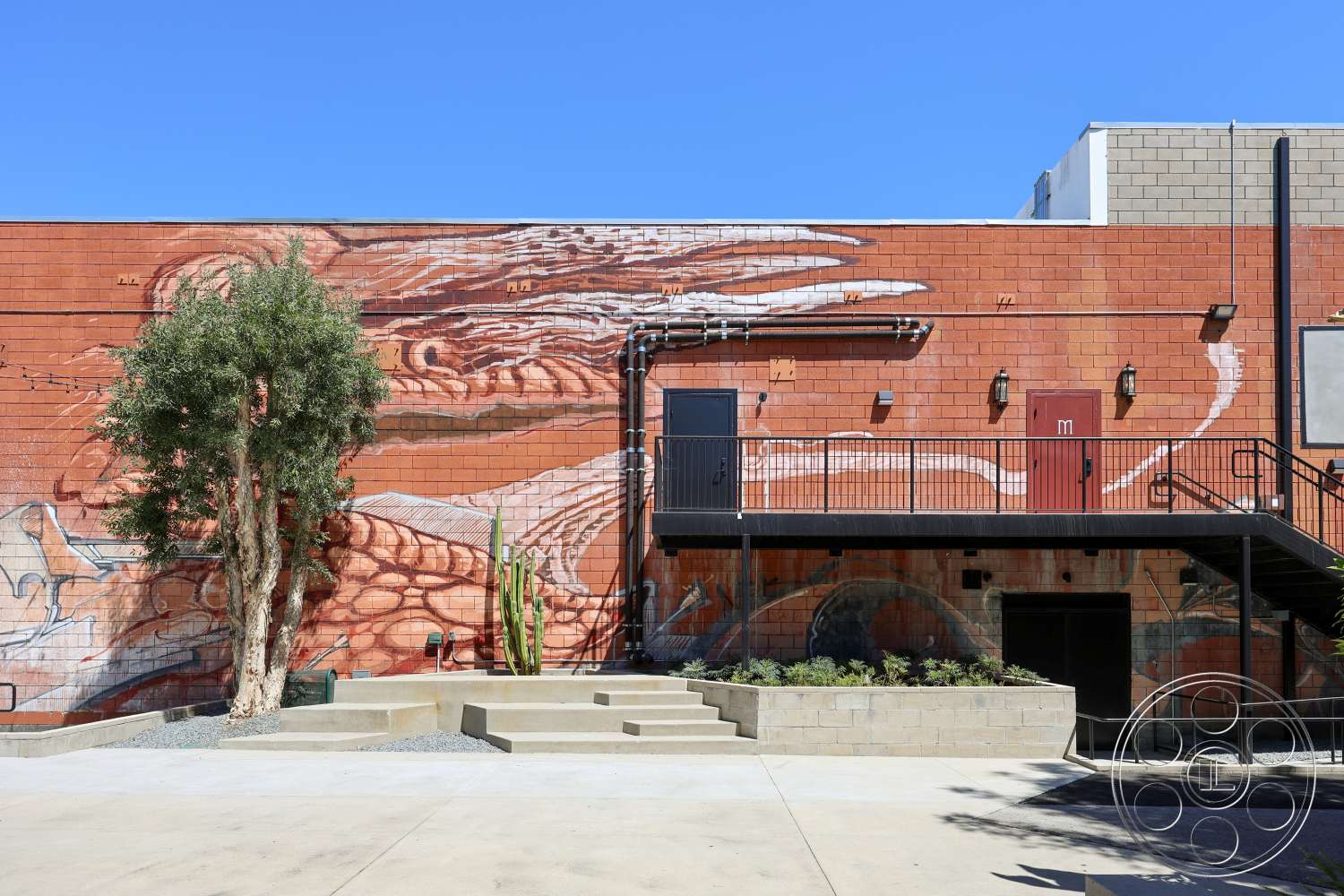 Club 74 - exterior, urban setting, concrete steps, black metal railings, metal staircase, modern industrial style, stone garden border, red painted concrete block walls, decorative mural artwork, landscaped garden with various plants, gray gravel flooring
