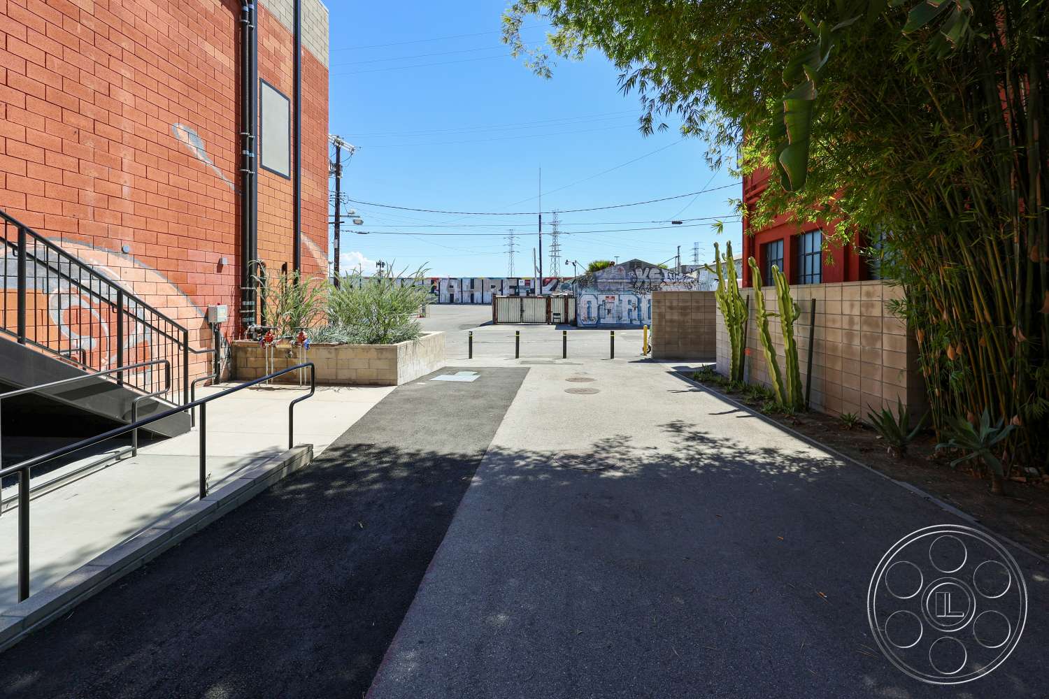 Club 74 - exterior, industrial architecture, concrete planters, asphalt driveway, modern urban setting, concrete sidewalk, metal stair railings, red brick building facade, tall bamboo plants, graffiti artwork