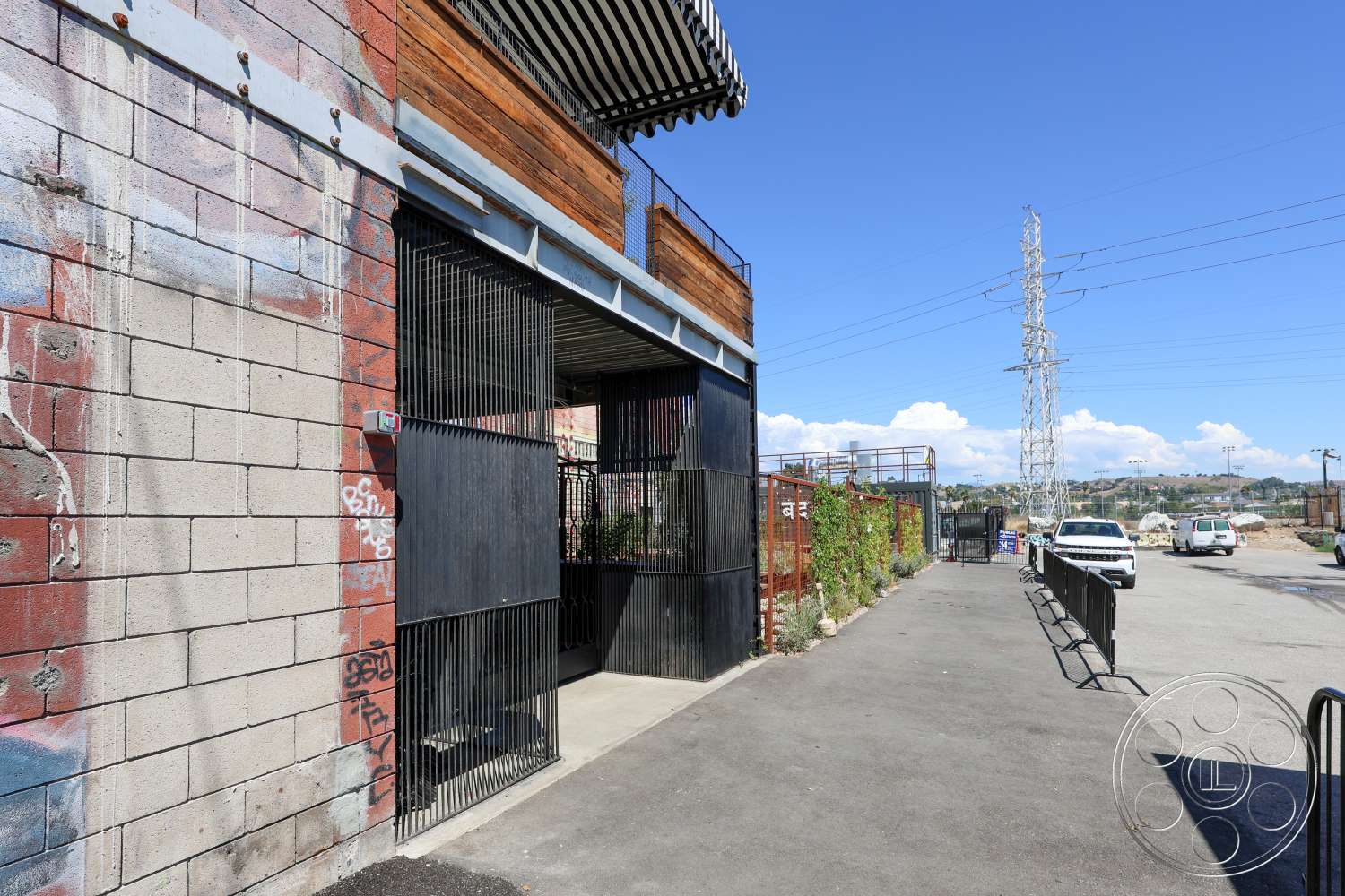 Club 74 - exterior, concrete block walls, urban setting, exposed brick wall, wooden overhang, landscaped pathway, industrial style architecture, paved parking area, linear plant beds, black metal fencing, corrugated metal roof, power lines in background