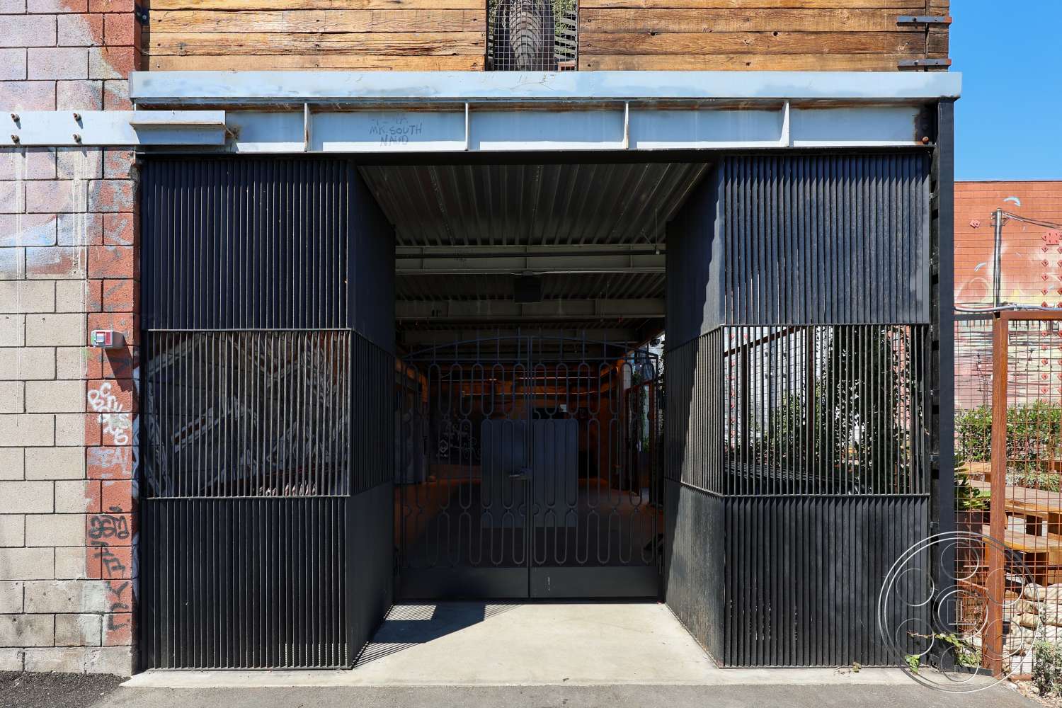 Club 74 - exposed wooden beams, urban setting, textured wall treatment, graffiti art, concrete block wall, steel gate, modern architectural details, landscaped outdoor area, industrial exterior, corrugated metal roof, metal grating, entrance facade, hardscaped path