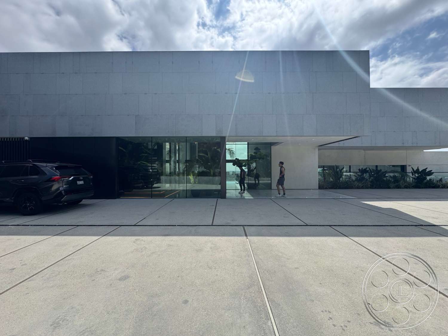 The Bellagio Estate - exterior, large floor-to-ceiling windows, white stone facade, flat roof design, minimalist architectural style, glass entrance doors, planter boxes with greenery, polished concrete driveway, slab concrete walkway