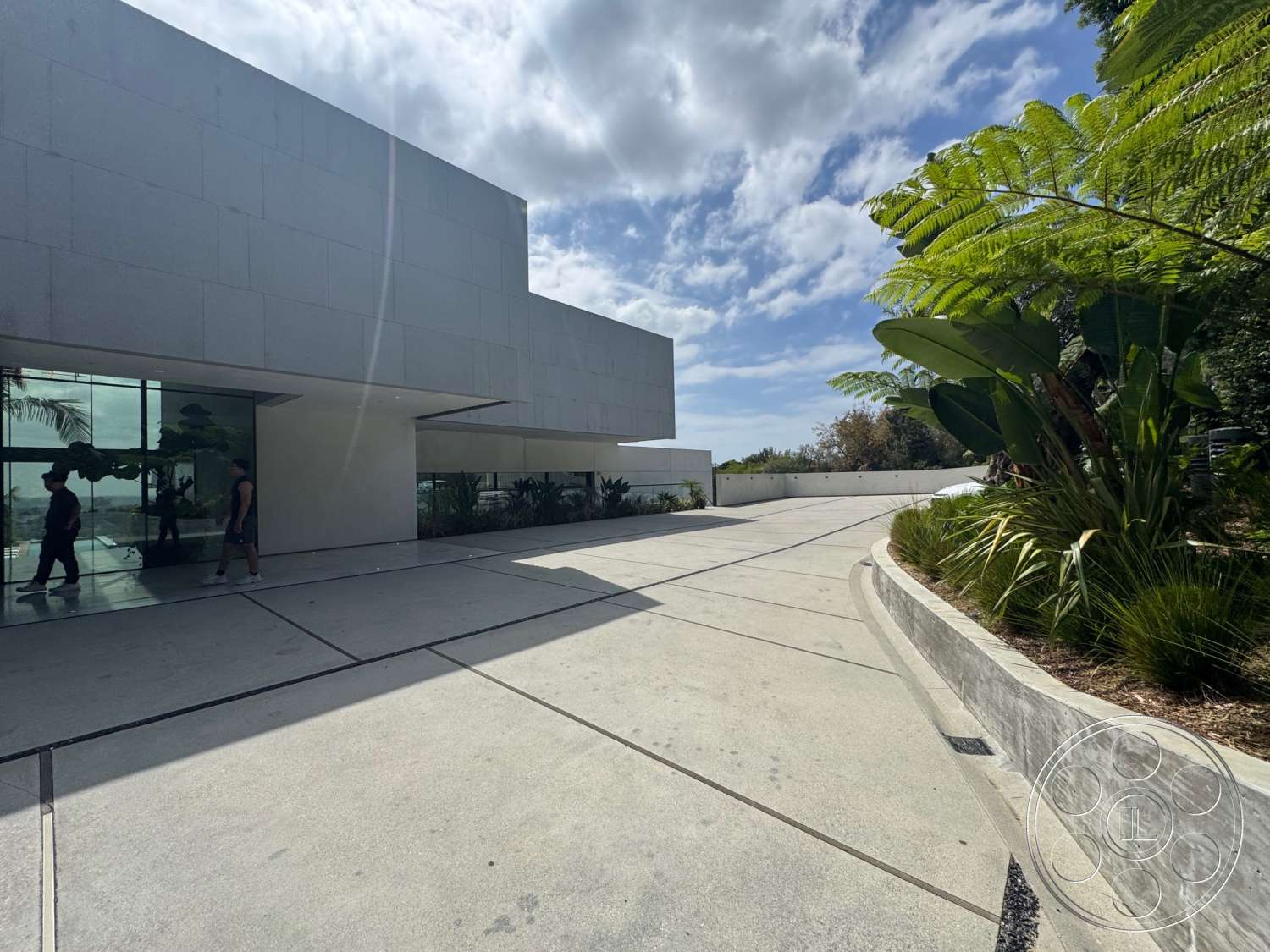 The Bellagio Estate - exterior, modern design, geometric shapes, concrete driveway, clear blue sky, tropical foliage, stucco wall, architectural landscaping, floor-to-ceiling glass windows, rectangular driveway, curved planter beds, horizontal wall panels, sculptural greenery