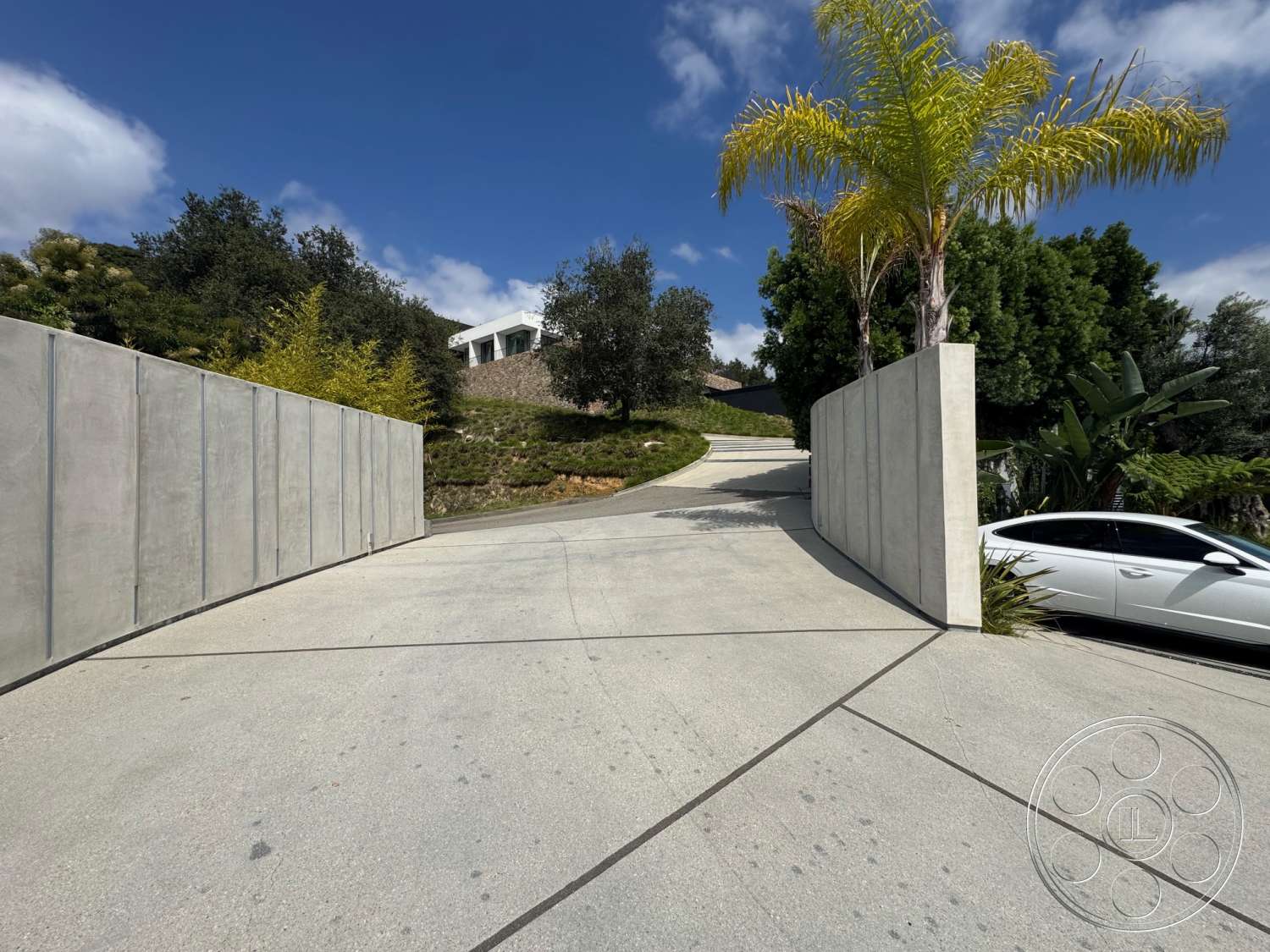 The Bellagio Estate - exterior, palm trees, modern architectural style, concrete driveway, curved driveway, tropical landscaping, hedge borders, steep hillside location, concrete privacy walls, house on elevation