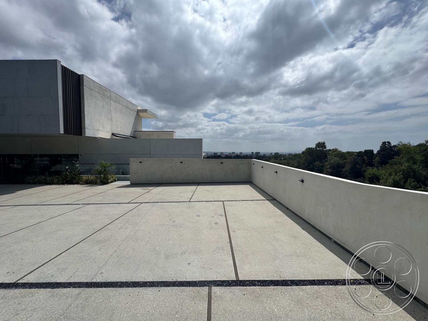 The Bellagio Estate - exterior, minimalist aesthetic, landscaped greenery, concrete wall, modern architectural style, skyline view, horizontal wood slats, large glass panels, flat roof design, cloudy sky backdrop, concrete terrace flooring