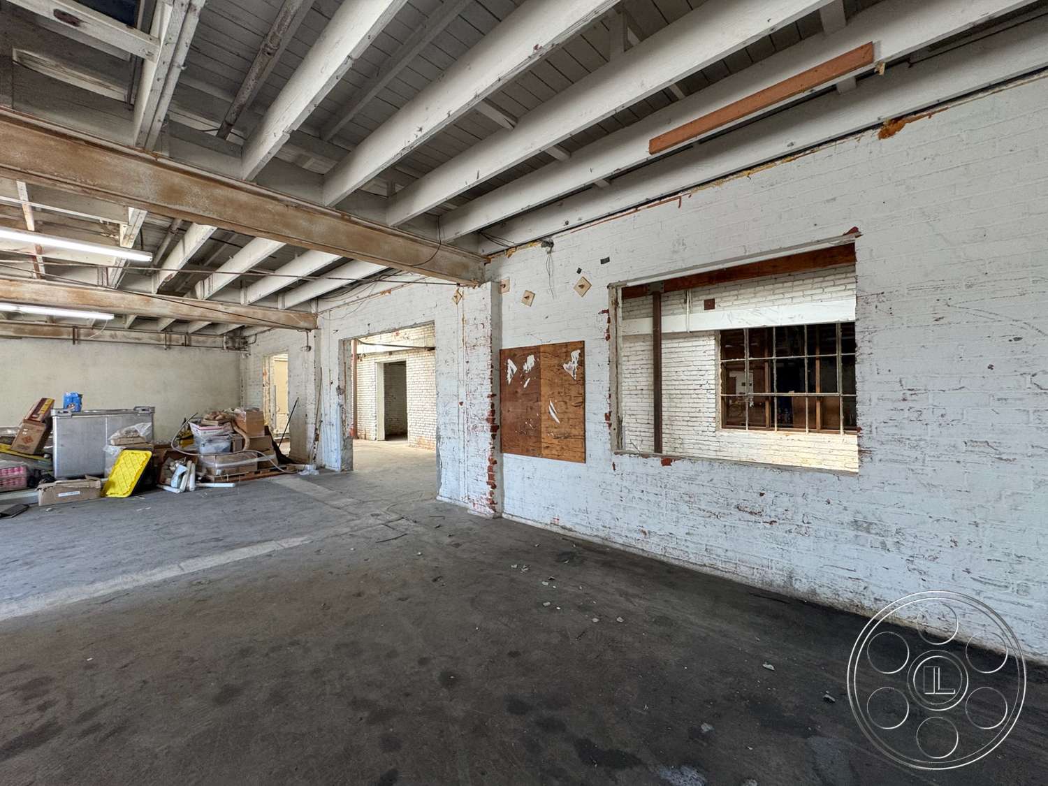 Warehouse 62 - large windows, open floor plan, concrete floor, vaulted ceiling, unfinished space, natural light flooding, exposed wood ceiling beams, industrial interior, white painted brick walls