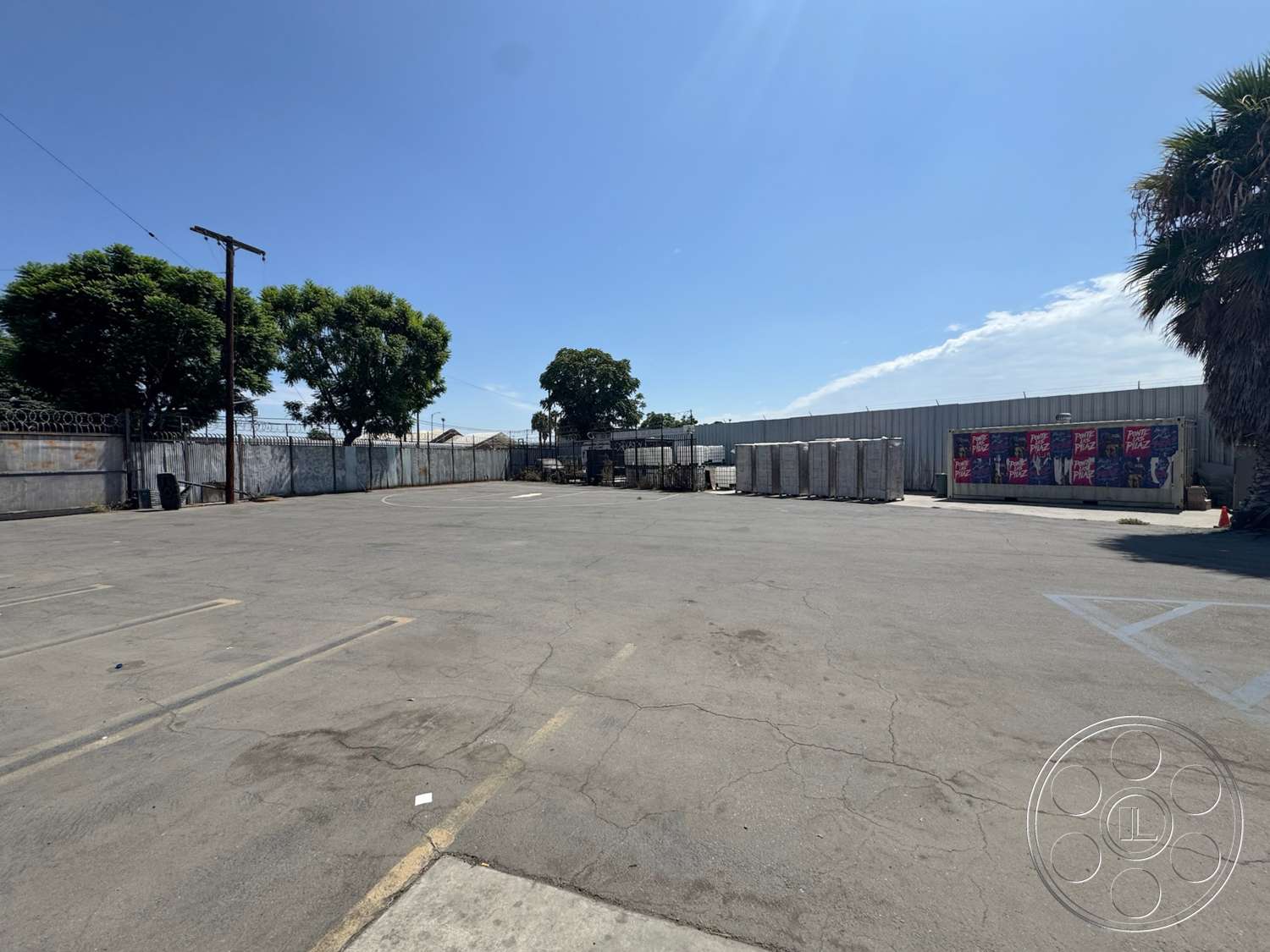 Warehouse 62 - palm trees, open space, urban setting, chain-link fence, asphalt parking lot, sunny outdoor environment, metal storage containers, industrial backdrop