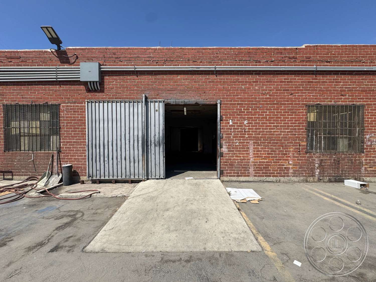 Warehouse 62 - exterior, asphalt driveway, red brick wall, industrial style architecture, metal sliding door, concrete loading dock, black window grilles, exposed utility piping, commercial warehouse entrance, plain concrete surface
