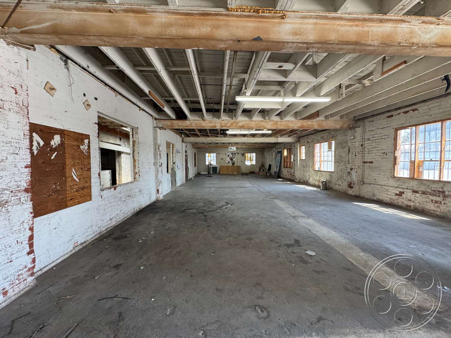 Warehouse 62 - large windows, natural light, open floor plan, concrete floor, exposed brick walls, unfinished ceiling, industrial-style interior, weathered wood beams, urban warehouse setting, plywood window coverings