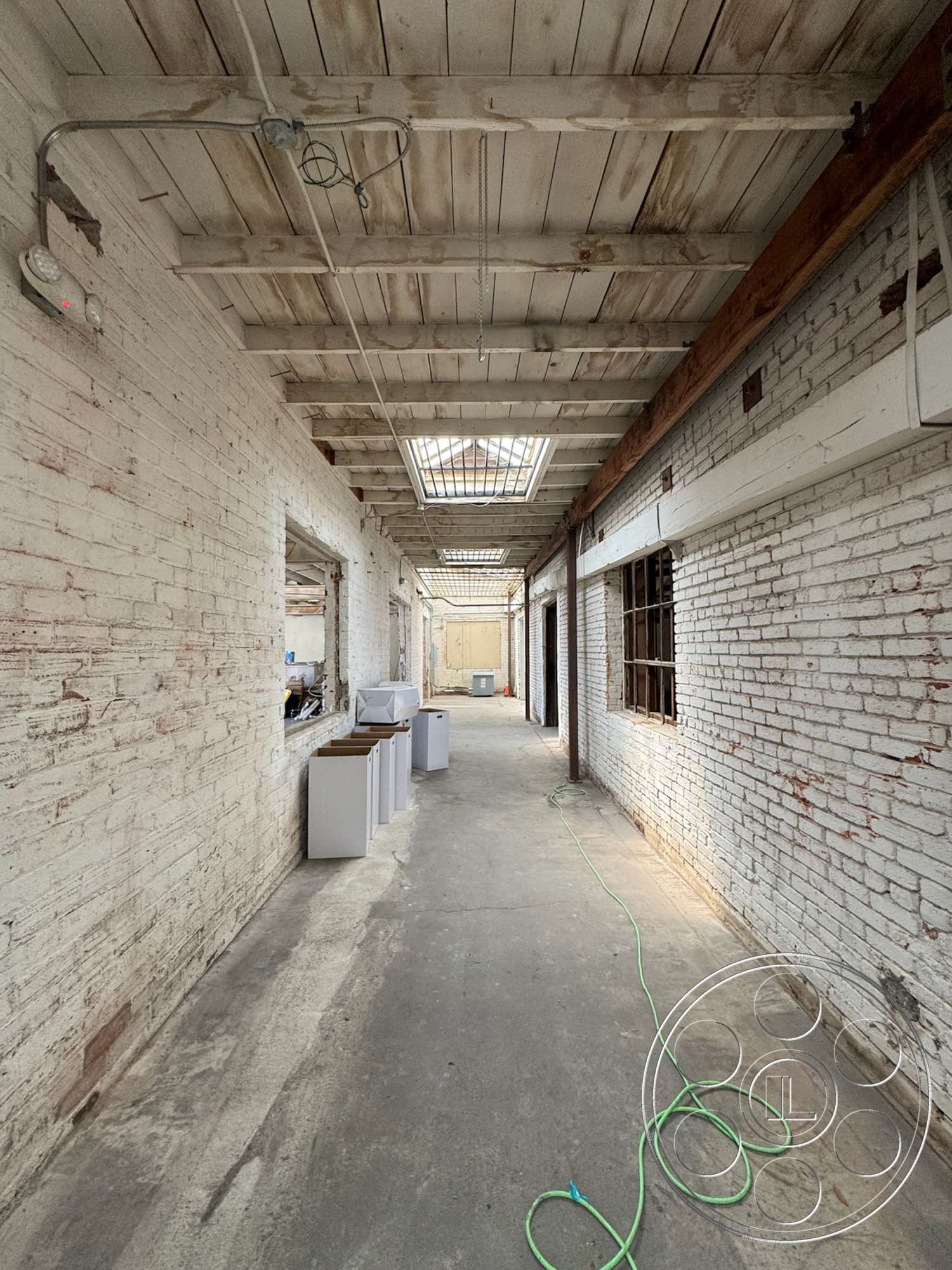 Warehouse 62 - transom windows, concrete floor, industrial style, exposed brick walls, unfinished space, white painted brick, wood beam ceiling, interior corridor, sky light windows, plumbing conduit