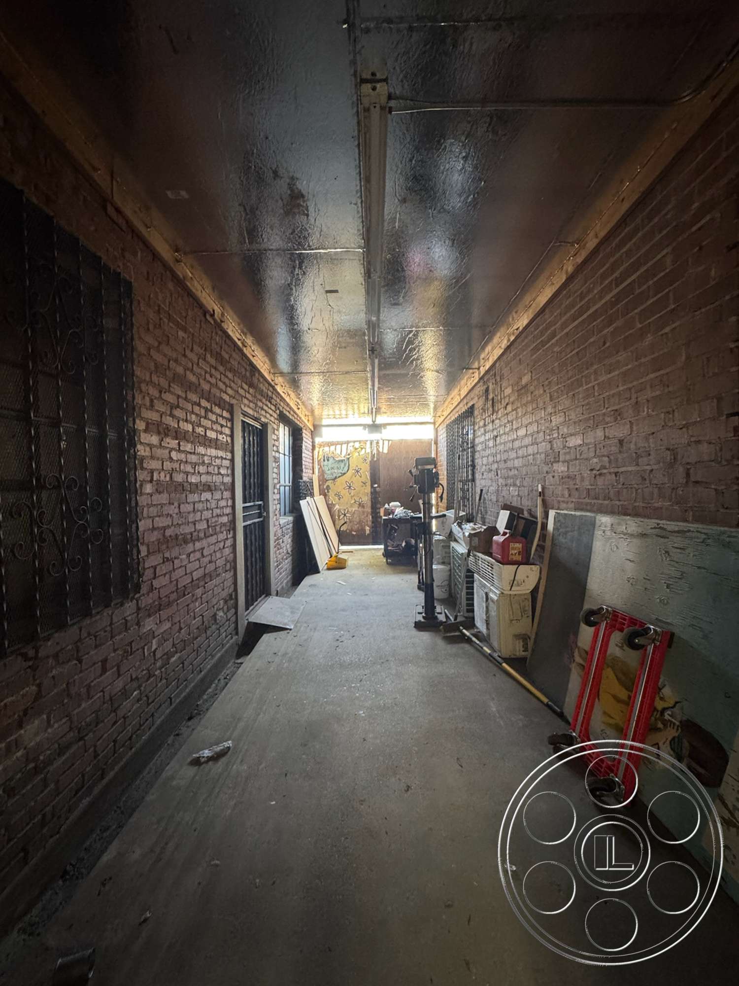 Warehouse 62 - concrete floor, exposed brick walls, industrial lighting fixtures, distressed wood accents, storage area, metal ceiling, interior hallway, long narrow corridor, security window grilles