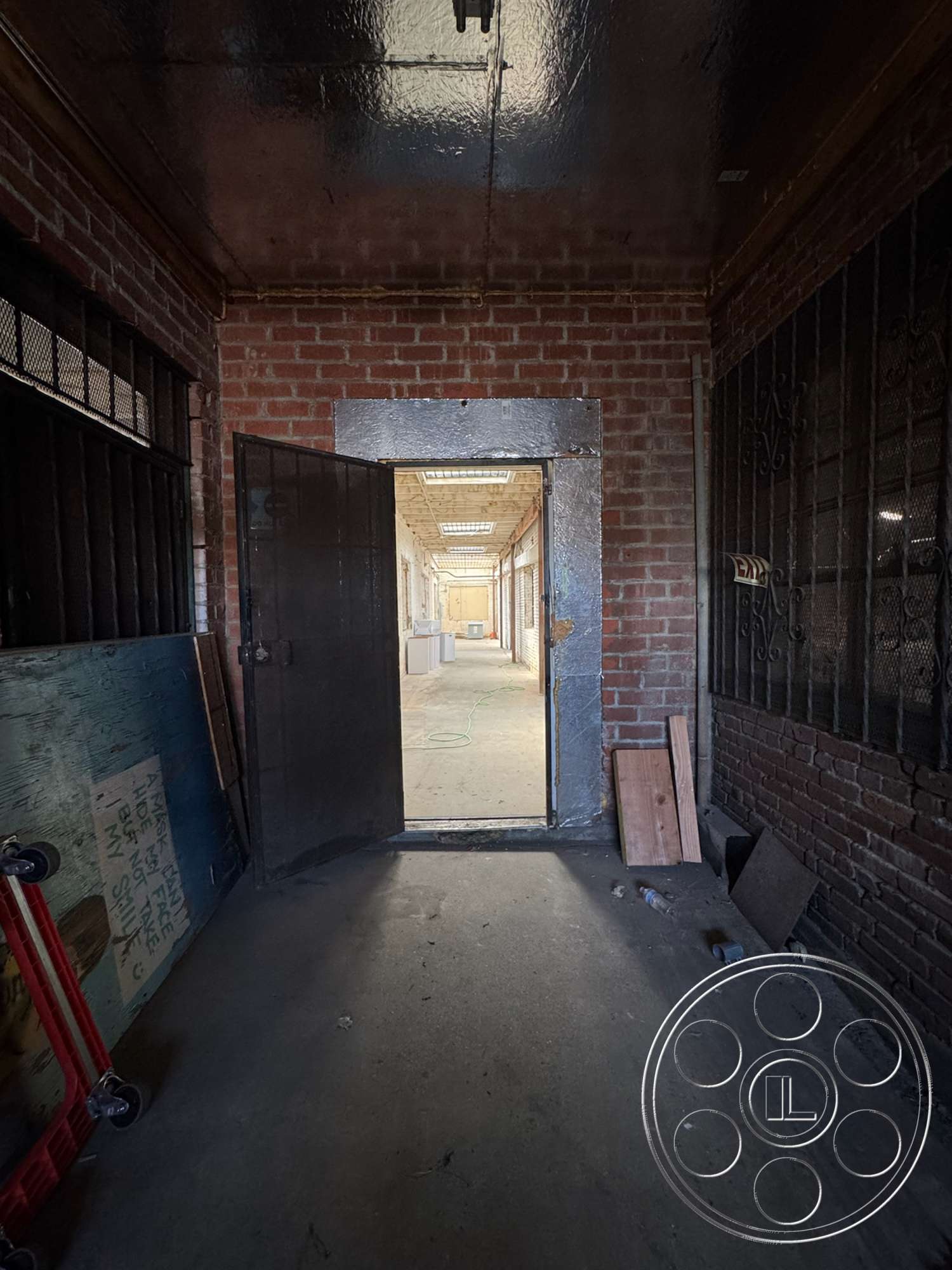 Warehouse 62 - concrete floor, exposed brick walls, metal door, natural light from skylights, metal door frame, interior corridor, industrial hallway, polished metal ceiling