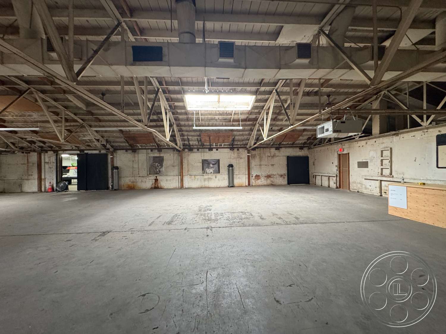 Warehouse 62 - minimalist design, open floor plan, concrete flooring, large open space, vaulted ceiling, skylight, commercial use, metal ductwork, urban loft setting, industrial interior, exposed wooden truss ceiling, whitewashed brick walls, wooden panel accent wall, warehouse-style space