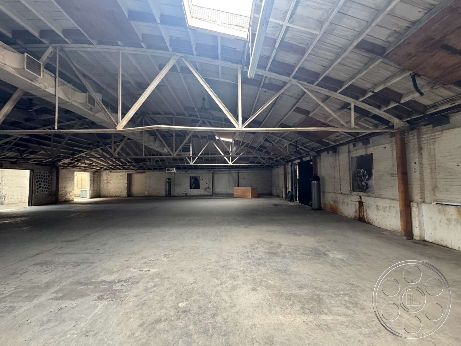 Warehouse 62 - concrete flooring, large open space, high vaulted ceiling, exposed wood ceiling beams, natural light from skylights, minimalist architectural details, industrial-style interior, warehouse setting, white painted brick walls, metal support trusses