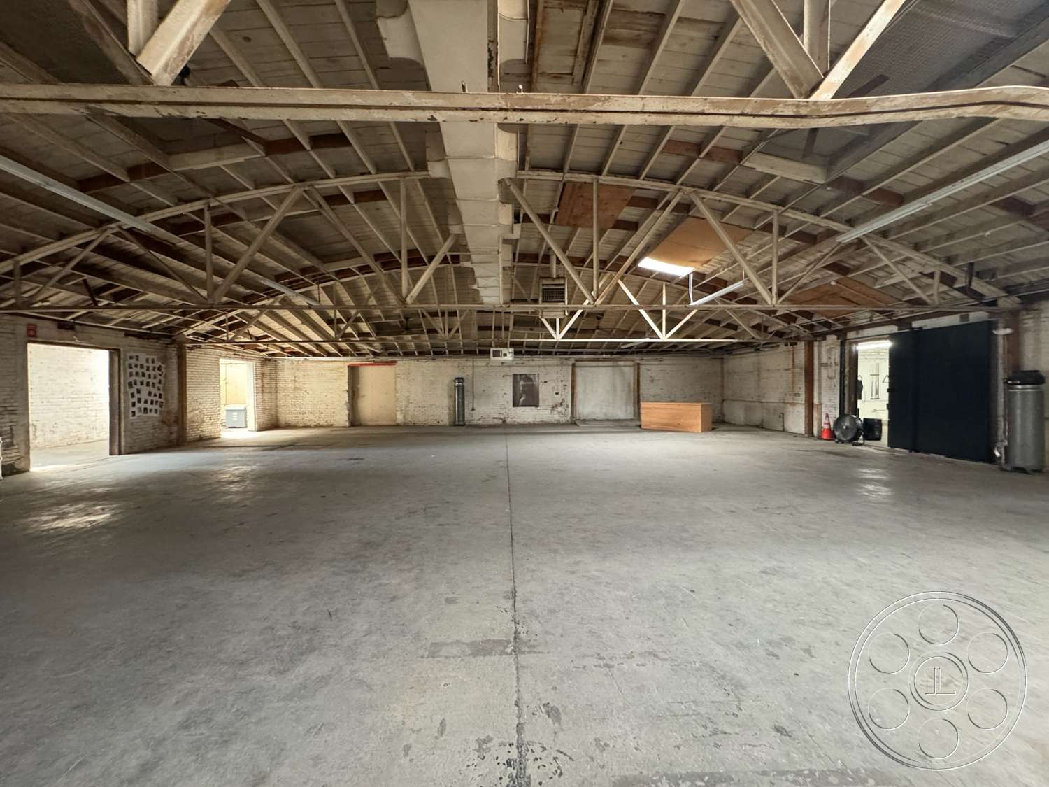 Warehouse 62 - concrete flooring, brick walls, vaulted ceiling, large arched windows, unfinished space, exposed wooden ceiling beams, exposed structural framework, open industrial interior, industrial design aesthetic