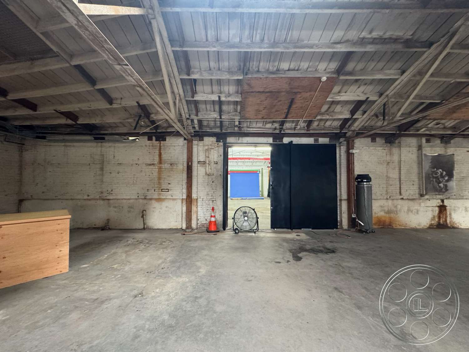 Warehouse 62 - open floor plan, concrete flooring, brick walls, natural light from windows, unfinished interior, industrial space, exposed wooden beams ceiling, large black doors, pedestrian access