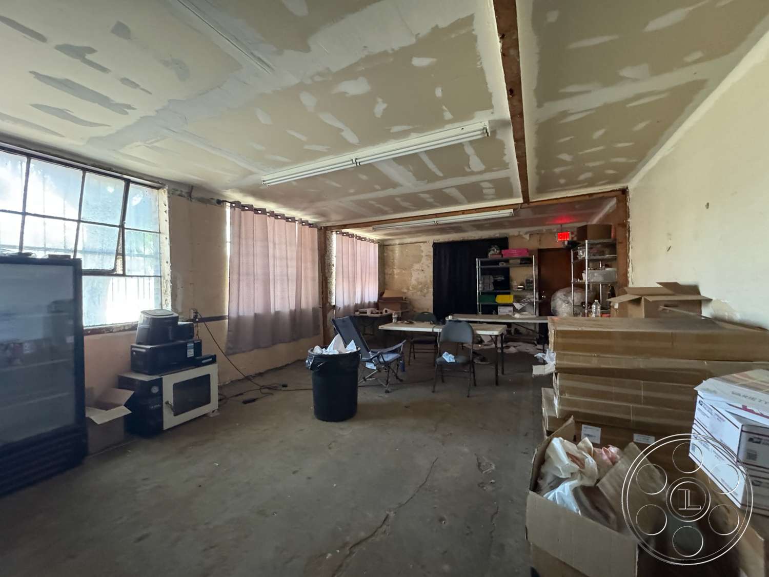 Warehouse 62 - concrete flooring, metal shelving unit, utility area, functional workspace, large industrial windows, plastic chairs, storage boxes, curtains for window treatment, sheetrock ceiling, unfinished drywall walls
