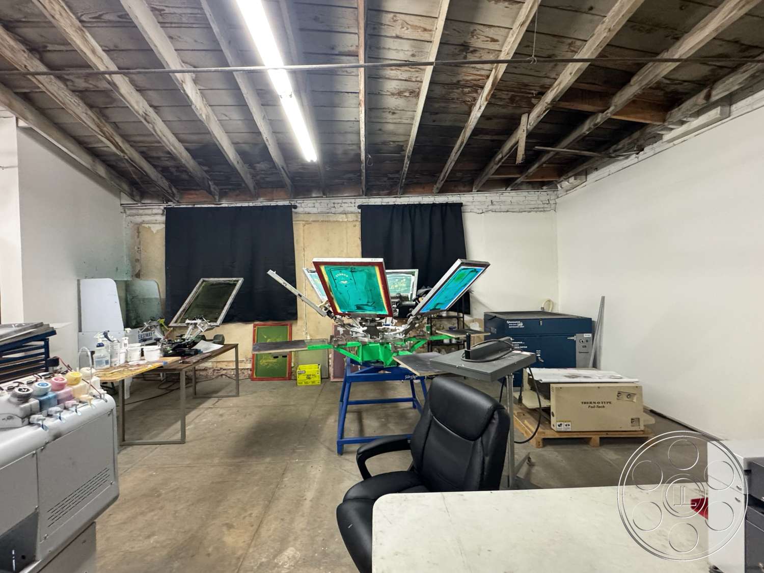 Warehouse 62 - concrete floor, black curtains, white painted walls, exposed wooden ceiling beams, wooden work tables, metal printing frames, plastic storage boxes, industrial workspace