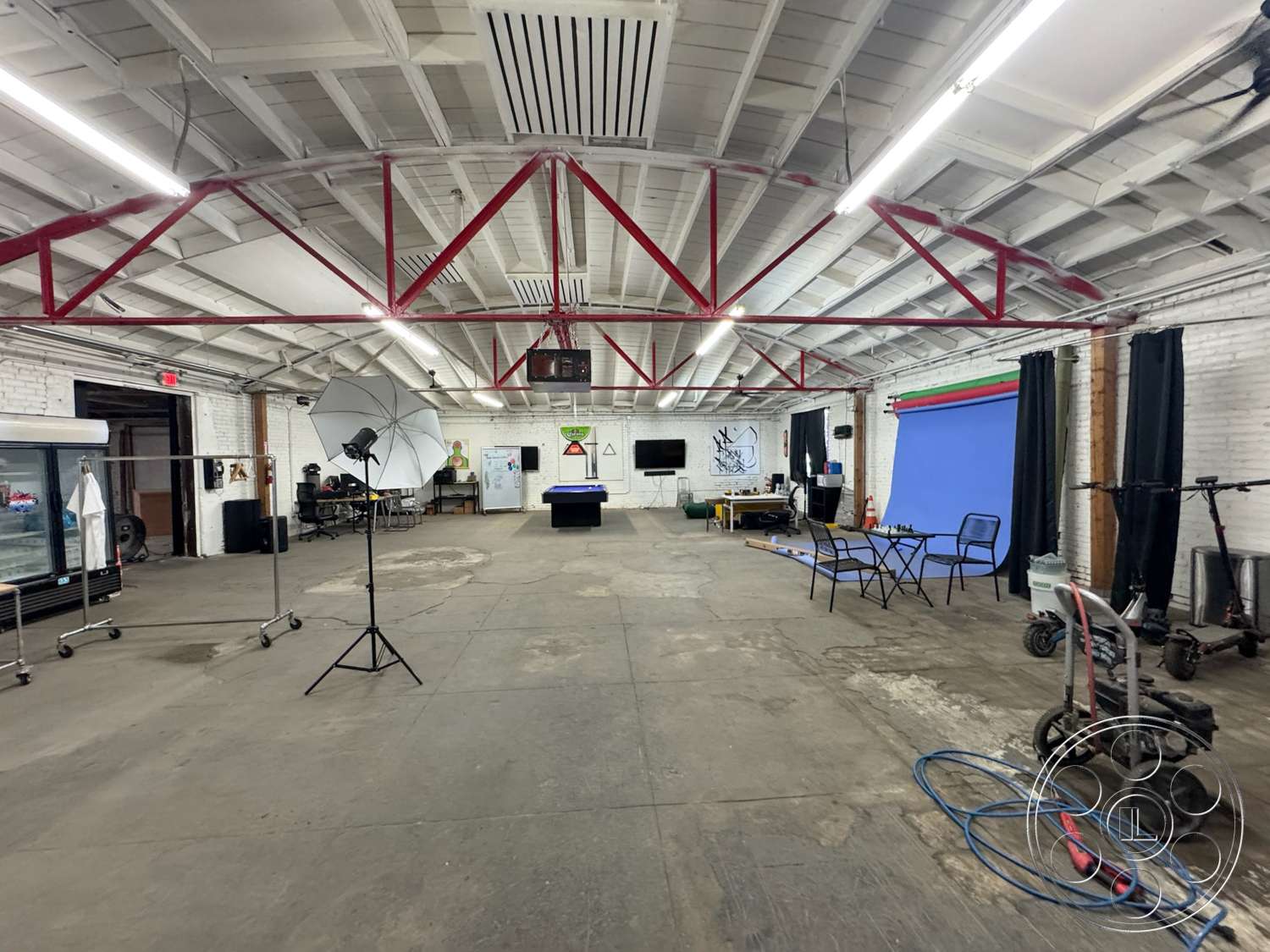 Warehouse 62 - concrete flooring, exposed brick walls, black curtains, large open area, industrial space, wood beam ceiling, white painted walls, red metal truss support structure, studio lighting setup, making space for multifunctional use