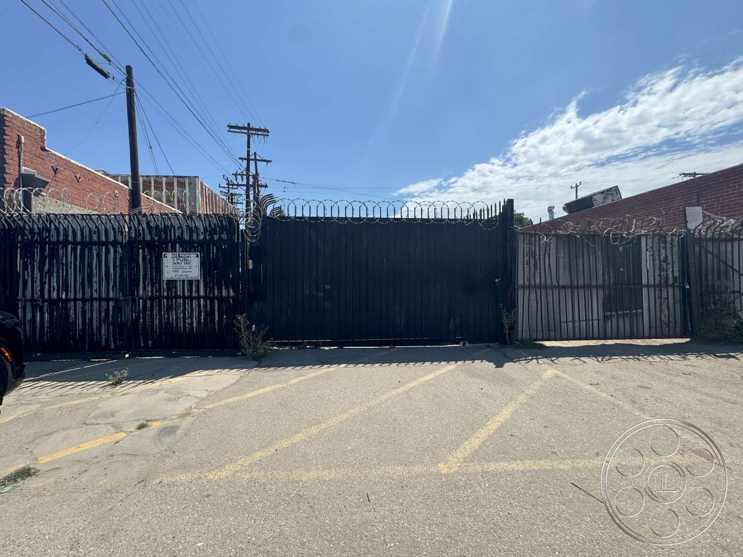 Warehouse 62 - exterior, asphalt surface, urban environment, concrete parking lot, industrial setting, metal security gate, barbed wire fencing, brick building exterior