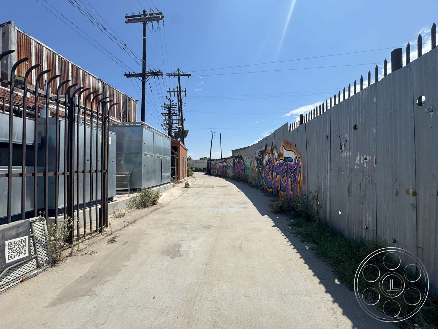 Warehouse 62 - exterior, urban environment, weathered wood, industrial setting, overhead power lines, glass storefront windows, corrugated metal fence, concrete alleyway, graffiti-covered wall, rusted metal siding, landscape debris