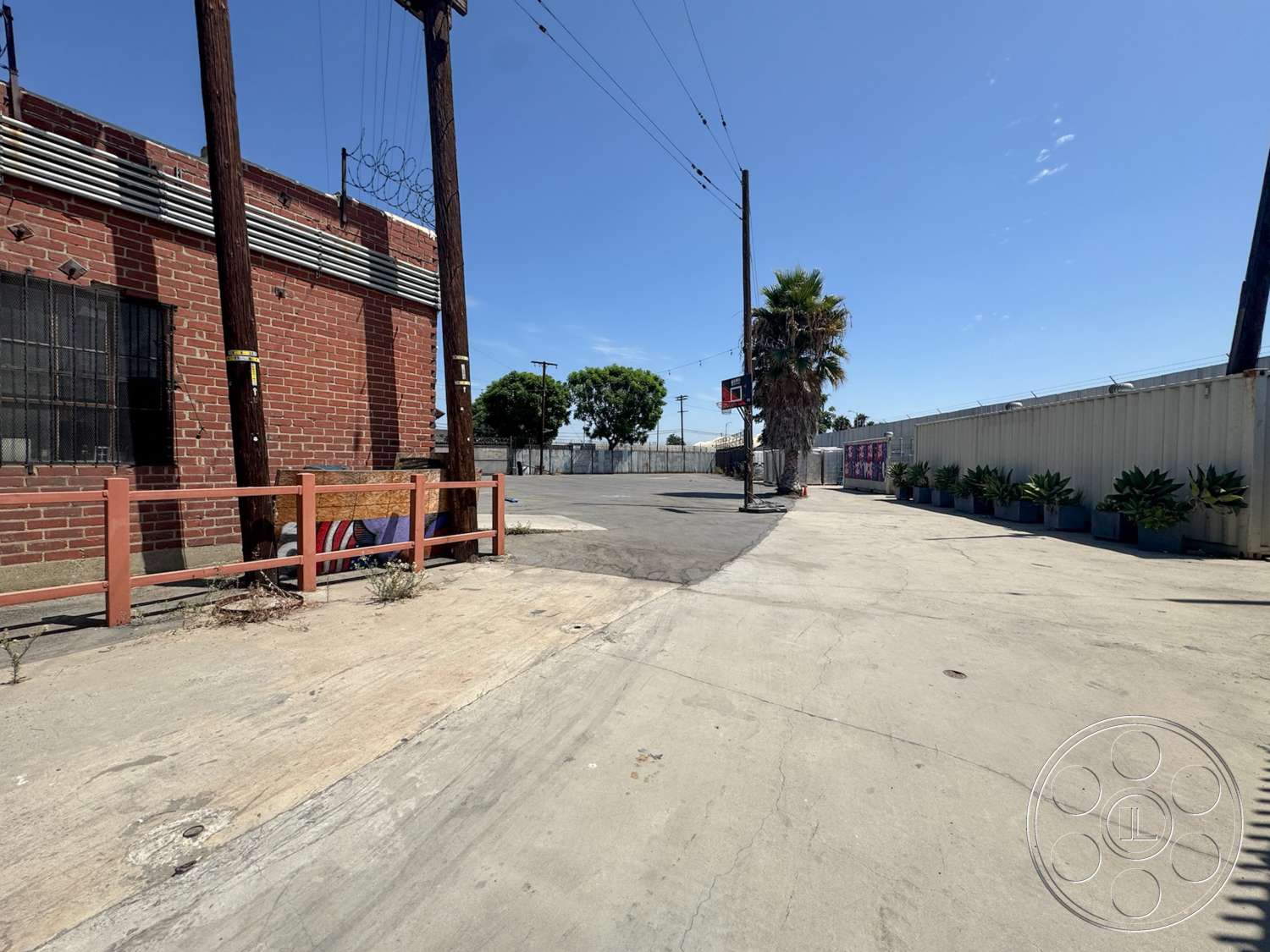 Warehouse 62 - potted plants, concrete pavement, urban setting, exposed brick wall, metal fencing, basketball hoop, clear blue sky, industrial exterior, wooden utility poles