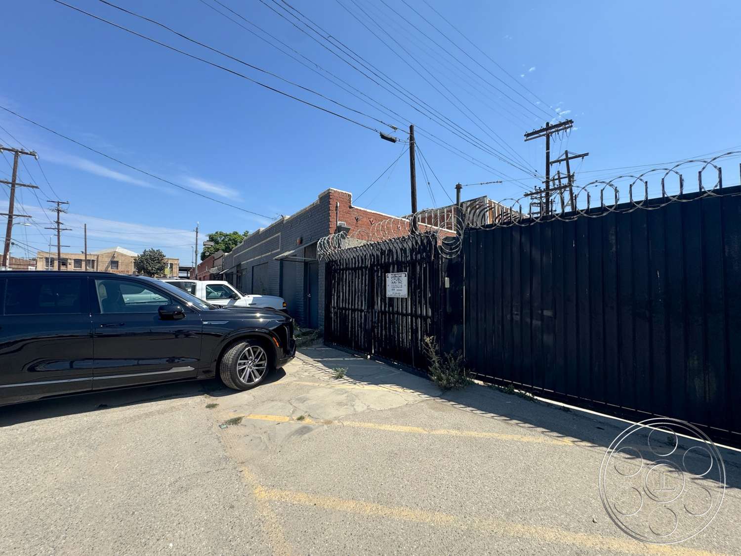 Warehouse 62 - exterior, concrete pavement, brick wall, urban environment, black metal gate, barbed wire fence, industrial setting, tarmac surface, steel power lines