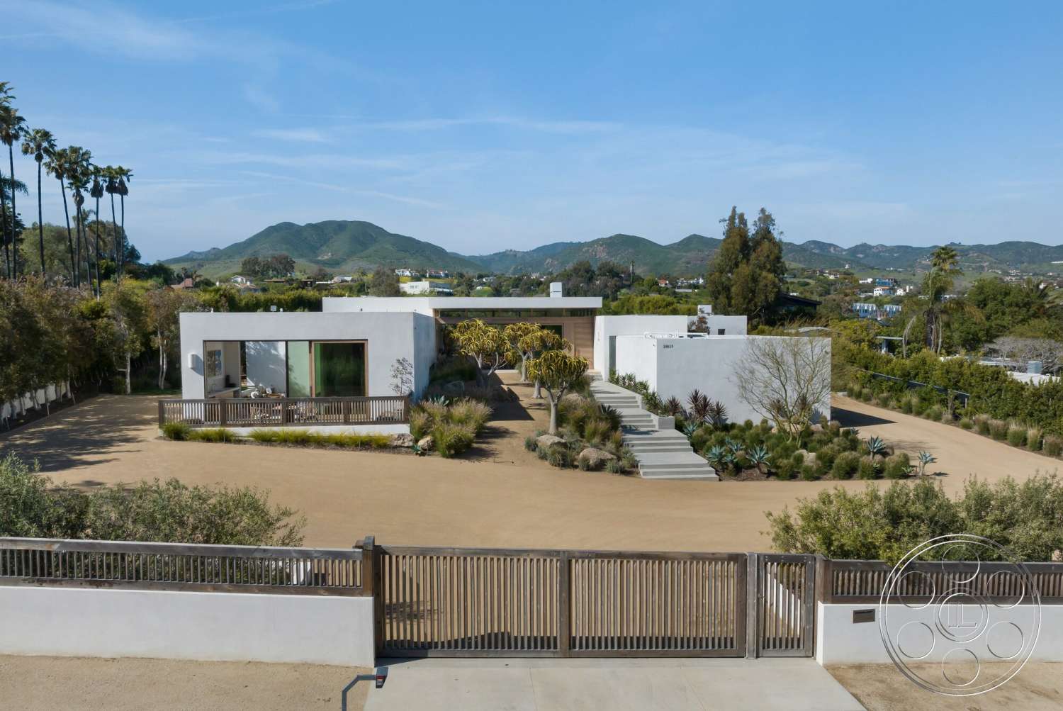 Modern 529 - large glass windows, concrete steps, single-story home, modern architectural style, concrete driveway, mountain view setting, exterior stucco walls, landscaped garden beds, planted palm trees, horizontal wood slat fence, sandy soil landscaping, interior visible living area, modern front entrance
