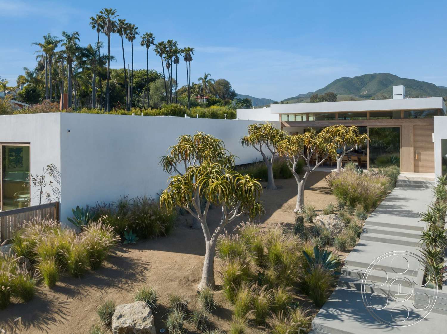 Modern 529 - exterior, white stucco walls, palm trees, concrete pathway, modern architectural style, mountain view, desert landscaping, outdoor garden, rock features, wooden front door, drought-resistant plants, low-maintenance shrubs, rectangular pathway, sloping site, grass and gravel areas