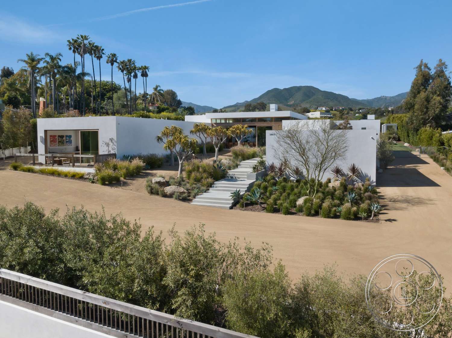 Modern 529 - exterior, natural stone accents, white stucco walls, open courtyard, large floor-to-ceiling windows, gravel driveway, flat roof design, wooden deck area, minimalist architectural style, palm trees in landscape, mountain view backdrop, concrete steps leading to entrance, landscaped garden with succulents