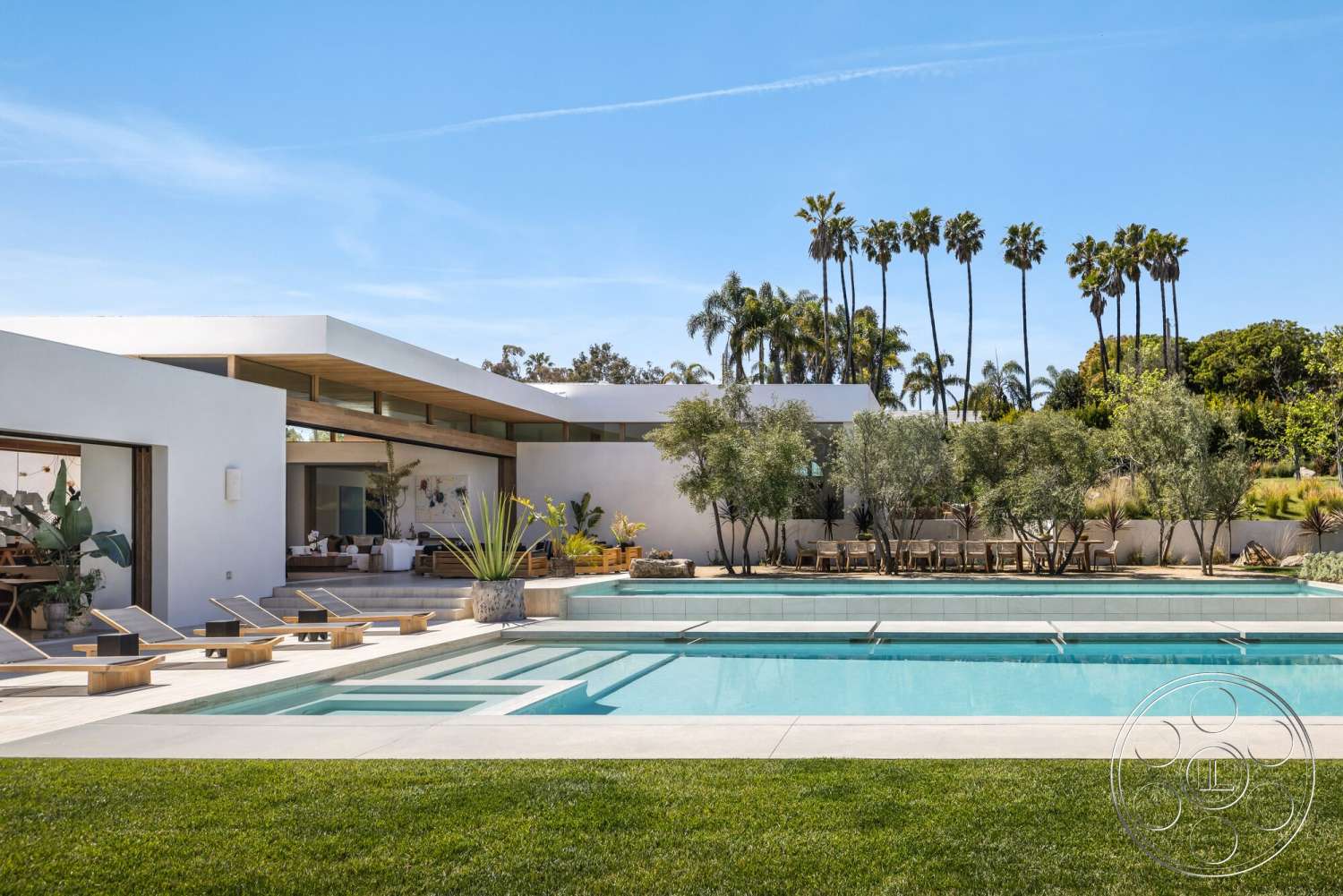 Modern 529 - exterior, white stucco walls, modern architecture, flat roof, minimalist design, glass sliding doors, rectangular swimming pool, outdoor dining area, concrete pool deck, wooden lounge chairs, concrete patio flooring, lawn with green grass, wood beam overhang, palms in background, tropical plants landscaping