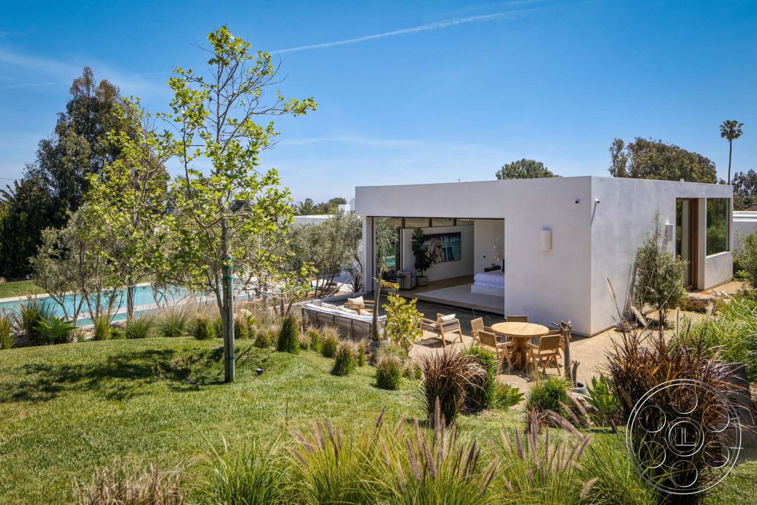Modern 529 - landscaped garden, white stucco walls, outdoor seating area, rectangular swimming pool, floor-to-ceiling windows, modern exterior, natural setting, open living space, residential backyard, green grass lawn, sunny environment, minimalist architectural style, concrete patio floor, wooden outdoor dining table, paved outdoor pathway