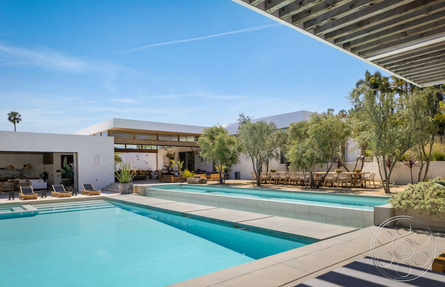 Modern 529 - white stucco walls, sliding glass doors, rectangular swimming pool, outdoor dining area, modern exterior, open concept living space, concrete pool deck, landscape trees, large format tiles, modern minimalist style, sunny outdoor environment, stone planter beds, interior kitchen view, wood beam patio cover