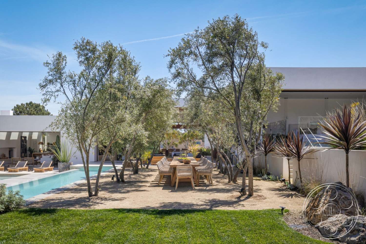 Modern 529 - neutral color palette, exterior, landscaped garden, low-maintenance landscaping, sliding glass doors, olive trees, spacious backyard, desert plants, rectangular pool, wooden lounge chairs, gravel patio flooring, concrete pool border, modern minimalist architecture, open-air dining area, clear blue sky view, sun-soaked outdoor space, wood outdoor dining table
