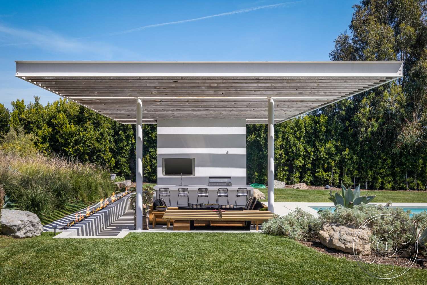 Modern 529 - exterior, landscaped garden, modern aesthetic, lush green lawn, rectangular pool, outdoor entertainment area, concrete patio flooring, low-maintenance vegetation, built-in outdoor seating, wood slatted pergola roof, striped outdoor lounge chairs, modern gas fire feature, smooth white stucco wall, indoor-outdoor living design