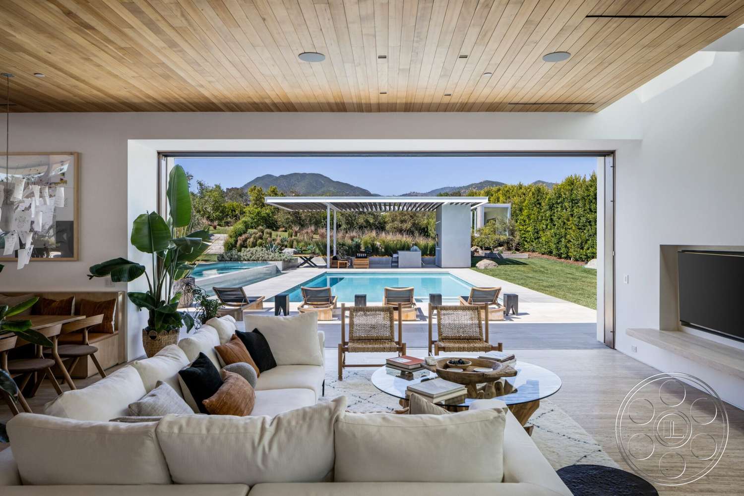 Modern 529 - neutral color palette, landscaped garden, modern furnishings, glass walls, exposed wooden beams, water feature, seamless indoor-outdoor transition, floor-to-ceiling windows, open-concept living space, wood ceiling panels, mountain view, woven outdoor chairs, concrete pool deck, rectangular pool, concrete patio floor, natural stone landscaping