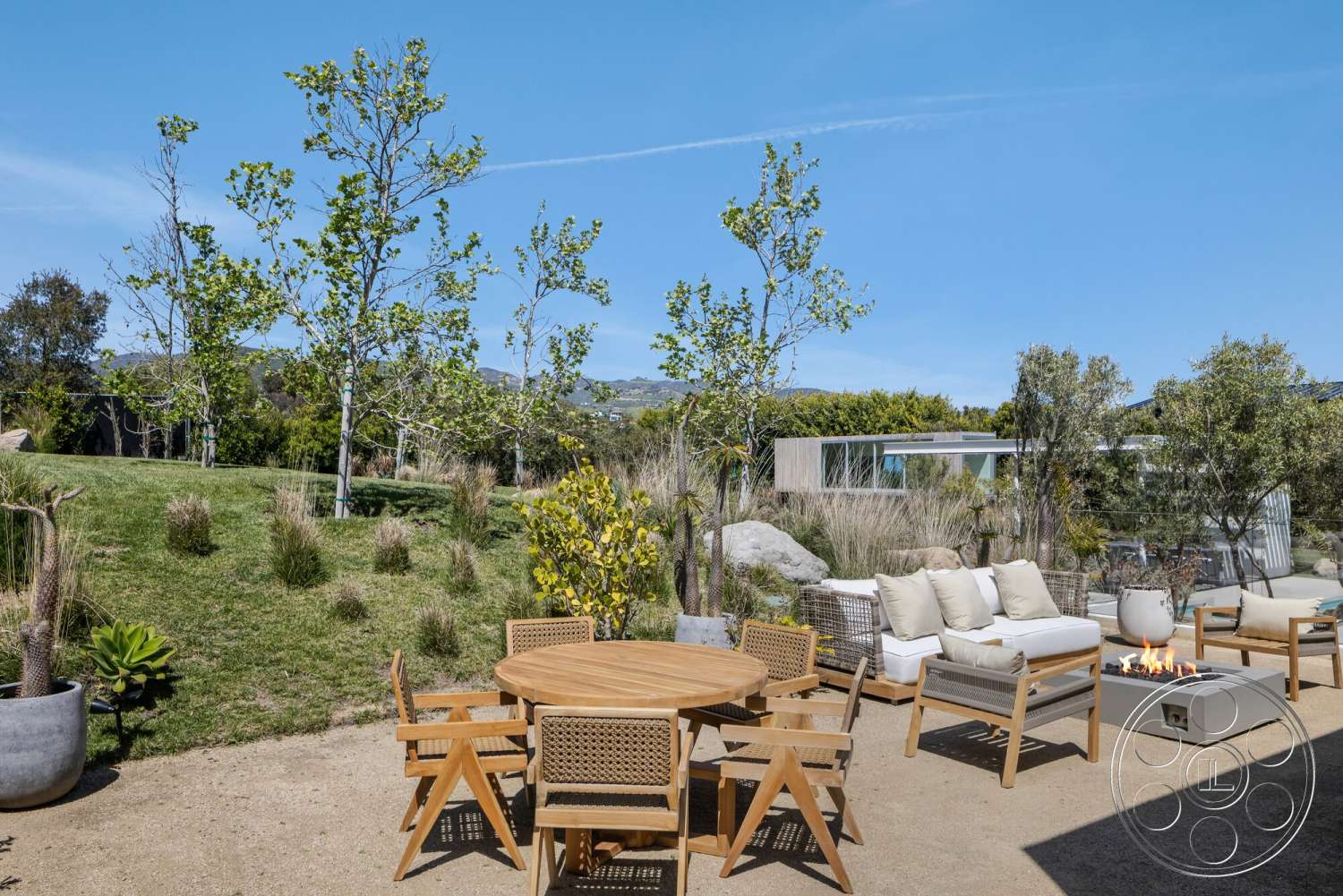 Modern 529 - exterior, lush greenery, glass windows, woven outdoor chairs, modern fire pit, leafy trees, minimalist outdoor seating area, natural stone landscaping, rolling hills view, contemporary landscape design, wood outdoor dining table, concrete fire pit surround, sandy patio ground