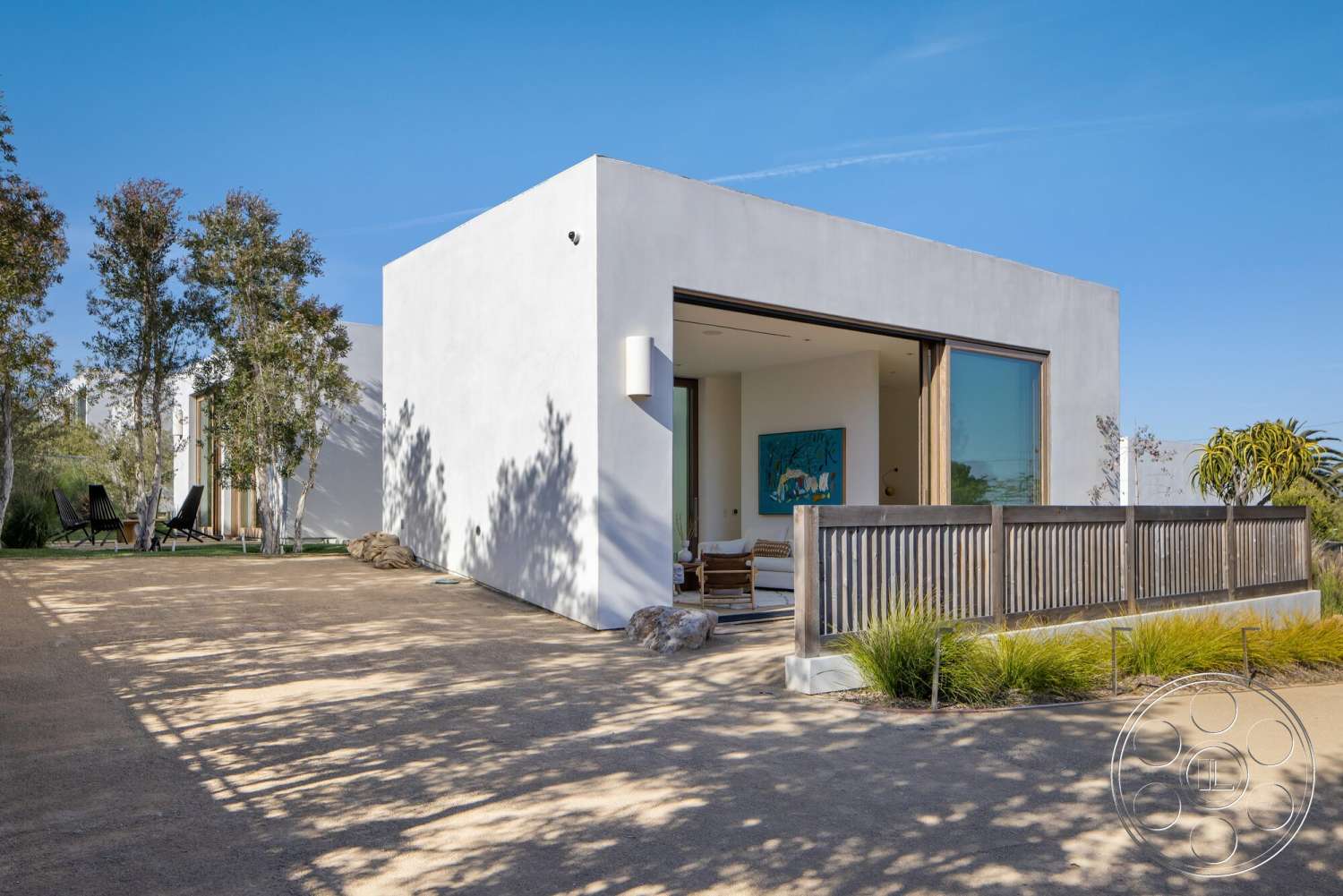 Modern 529 - exterior, outdoor seating area, flat roof design, landscaped garden setting, surrounding trees and shrubs, minimalist architectural style, concrete patio floor, large floor-to-ceiling glass windows, smooth white stucco walls, natural wood sliding doors, wooden railing fence, light gravel driveway