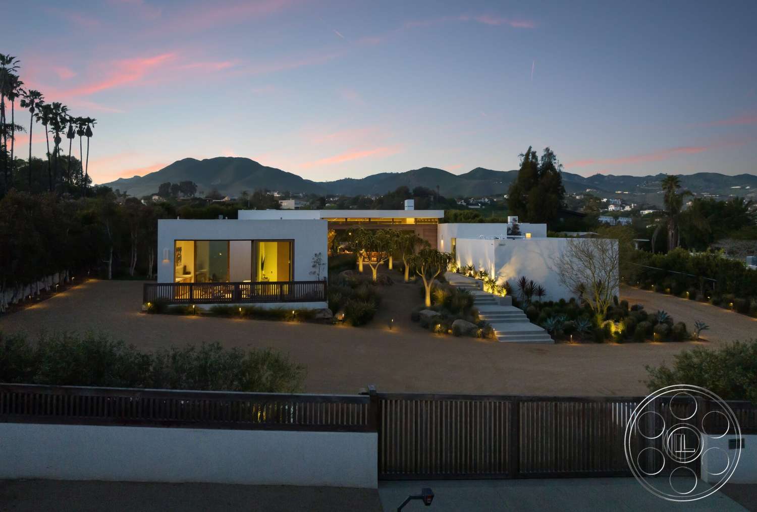 Modern 529 - exterior, white stucco walls, floor-to-ceiling windows, modern architectural style, outdoor lighting features, tropical palm trees, flat roof design, landscaped garden area, wood deck patio, desert plant landscaping, surrounding mountain view, staggered concrete steps, smooth gravel driveway