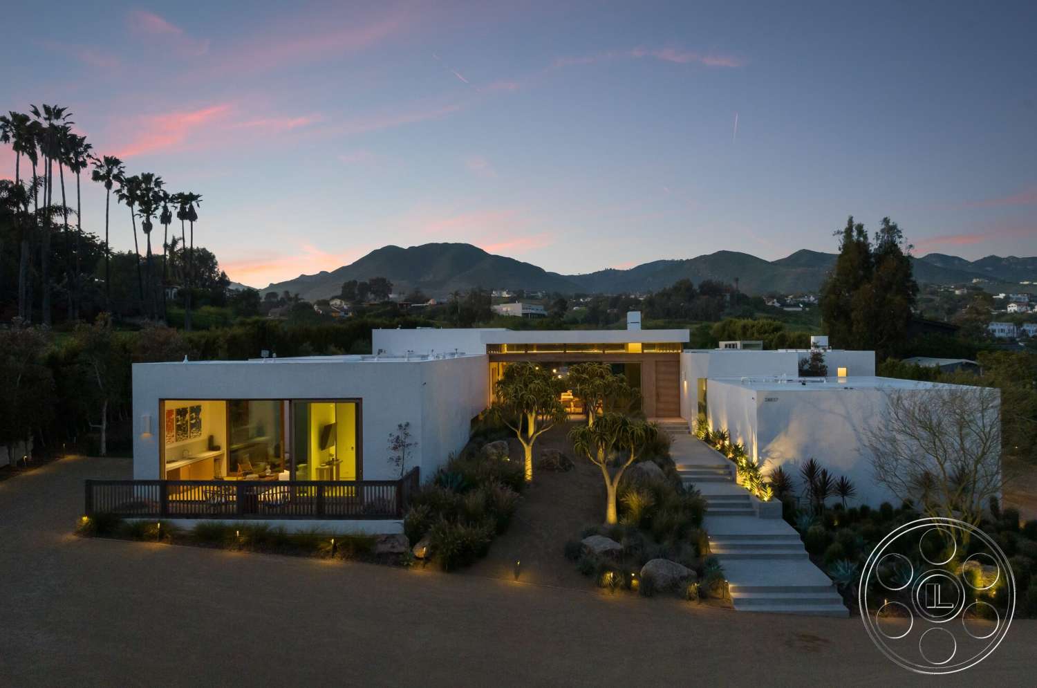 Modern 529 - paved driveway, white stucco walls, flat roof, large glass windows, tropical plants, single-story home, open courtyard, evening lighting, modern exterior, mountain view, concrete walkway, desert landscaping, wooden front door