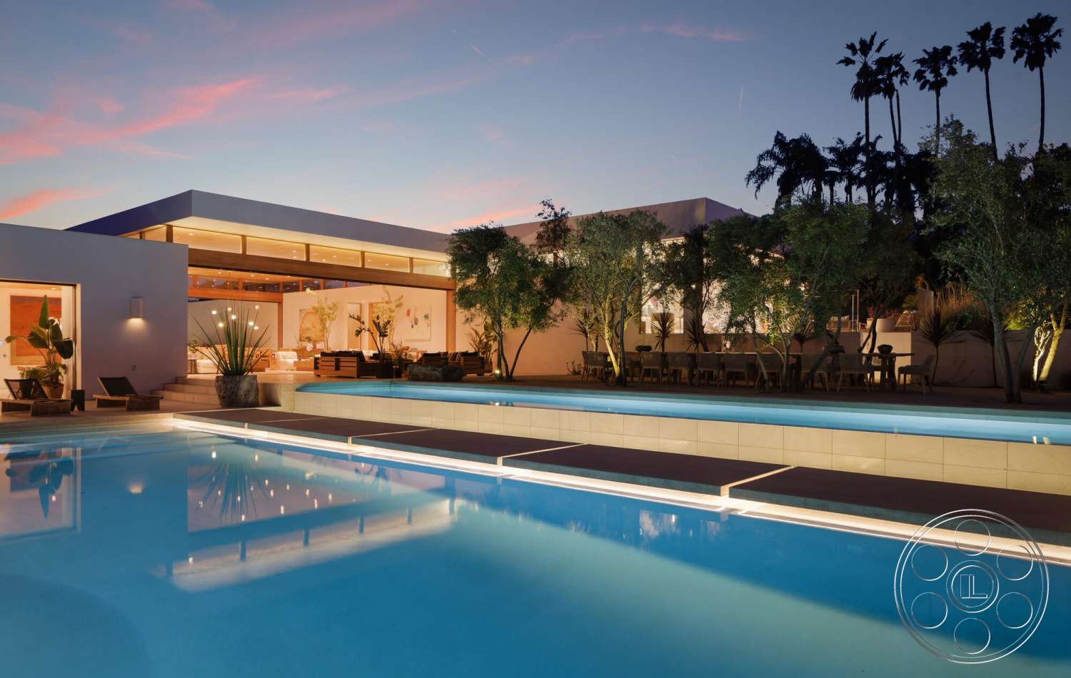 Modern 529 - exterior, white stucco walls, flat roof, outdoor dining area, modern architectural style, large floor-to-ceiling windows, concrete pool deck, rectangular pool, wooden patio furniture, surrounding vegetation, palm tree landscaping, nighttime lighting features