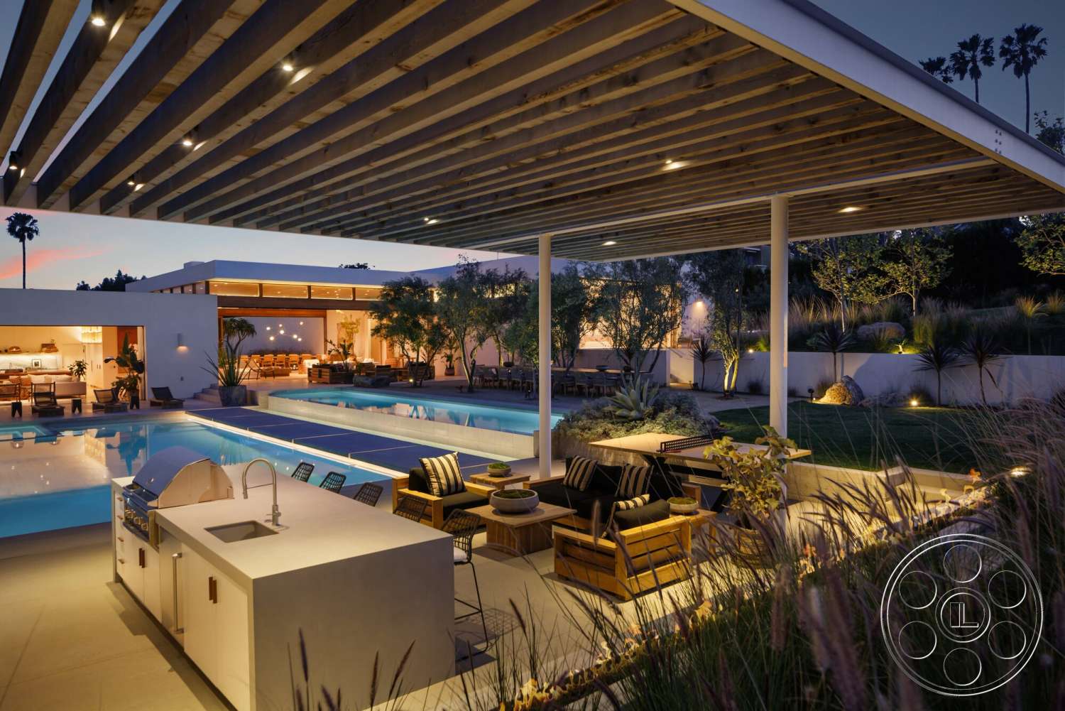 Modern 529 - exterior, landscaped garden, white stucco walls, potted plants, rectangular swimming pool, stainless steel grill, concrete pool deck, surrounding palm trees, luxury outdoor seating, wood beam ceiling, stone patio flooring, covered patio area, recessed outdoor lighting, modern outdoor kitchen, dusk setting with soft lighting