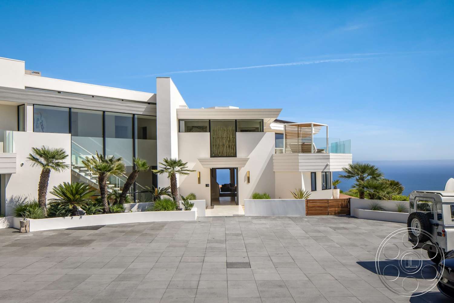 Modern 528 - exterior, white stucco walls, floor-to-ceiling windows, modern architectural style, palm landscaping, flat roof design, rectangular driveway, glass balcony railings, smooth concrete steps, wooden accent walls, stone paver driveway, ocean view setting