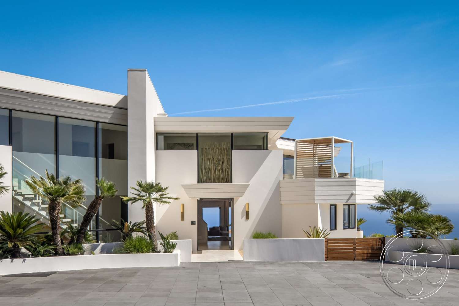 Modern 528 - large windows, natural light, modern exterior, tropical landscaping, bright blue sky, gated driveway, flat roof design, concrete patio flooring, stucco wall finish, minimalist architectural style, glass wall panels, glass entry doors, expansive ocean view, palm trees in garden, wood slatted balcony railing, open-plan entry, front entrance path