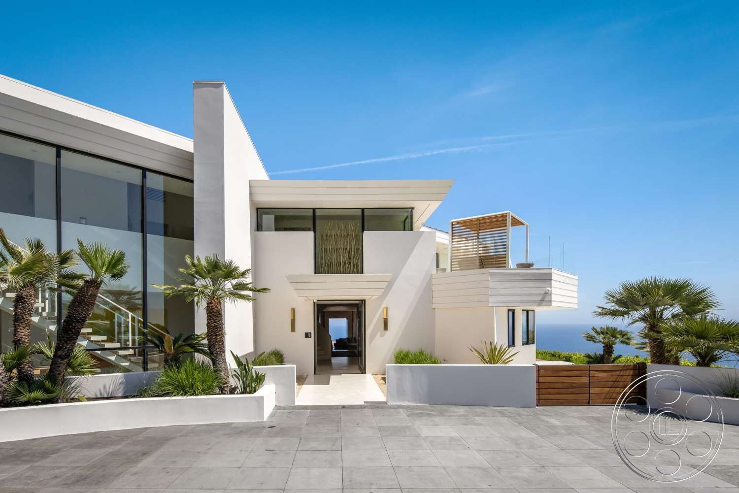 Modern 528 - exterior, palm trees, modern entryway, large glass windows, open staircase, ocean view, mountain backdrop, flat roof design, concrete patio flooring, minimalist architectural style, landscaped tropical garden, stone driveway pavers, white Stucco walls, horizontal wood slat balcony