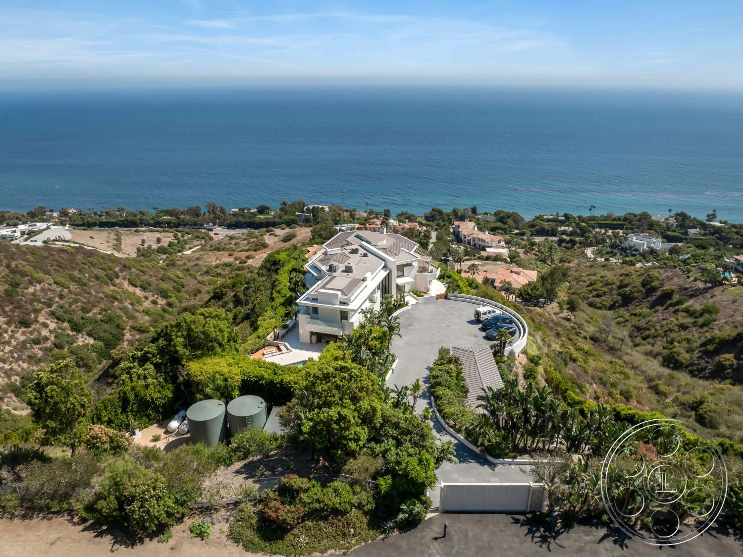 Modern 528 - exterior, flat roof, circular driveway, multi-story building, modern architectural style, ocean view, concrete driveway, hillside location, metal storage tanks, landscaped garden area