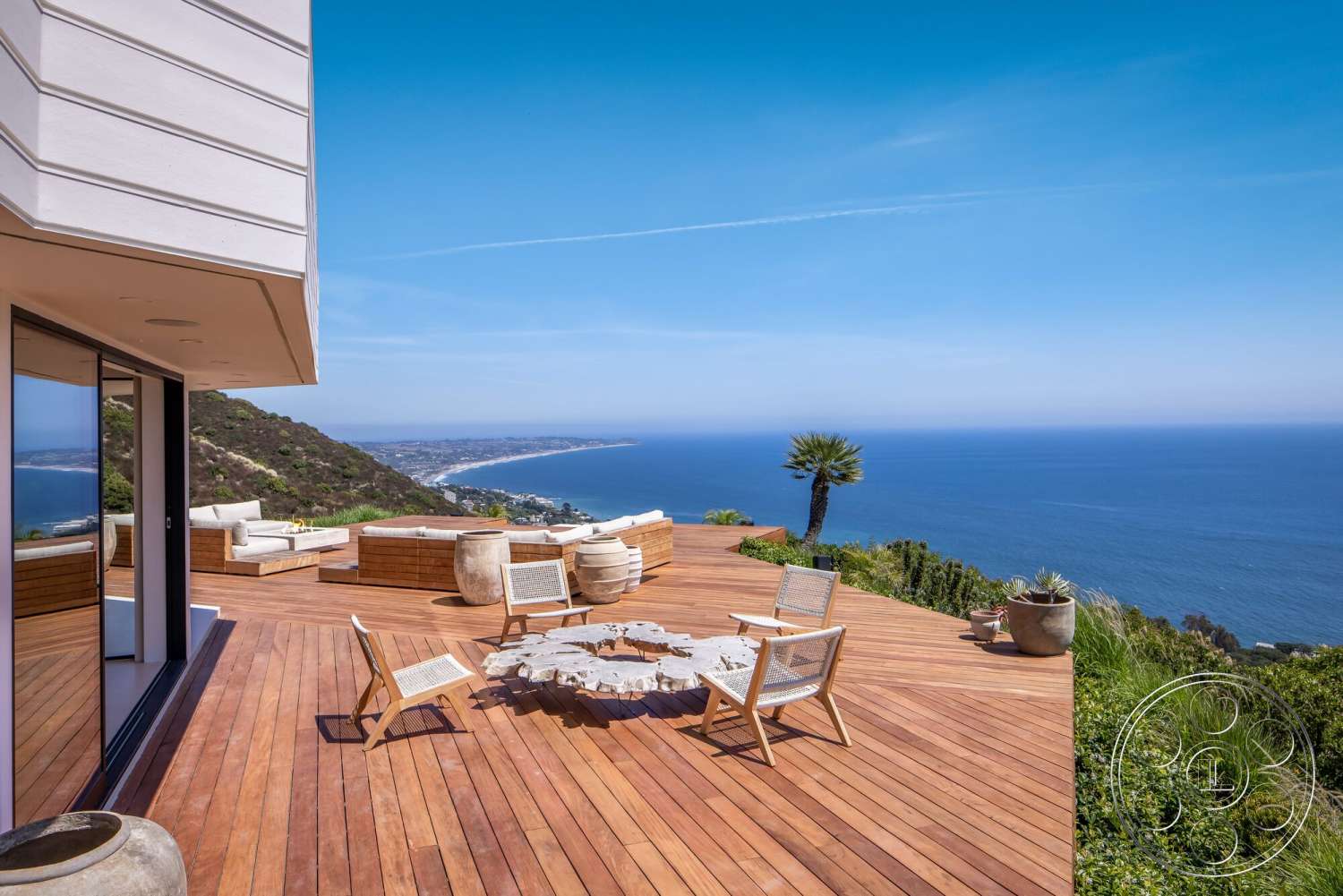 Modern 528 - exterior, open outdoor space, tropical landscaping, coastal setting, horizontal wood siding, textured concrete planters, modern lounge chairs, panoramic ocean view, contemporary home design, wood deck flooring, floor-to-ceiling glass doors, rectangular wooden dining table, fire pit seating area, green hillside backdrop