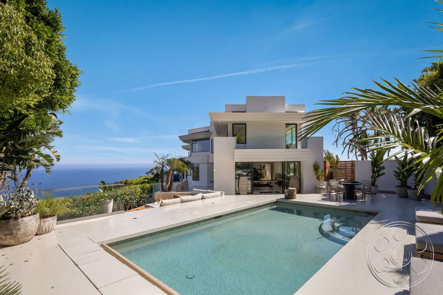 Modern 528 - exterior, white stucco walls, glass sliding doors, outdoor seating area, rectangular swimming pool, modern architectural style, ocean view, sunny coastal setting, flat roof design, landscaped garden area, concrete patio flooring, potted palm trees